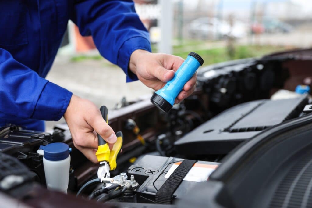 Mechanic with flashlight fixing car outdoors, closeup