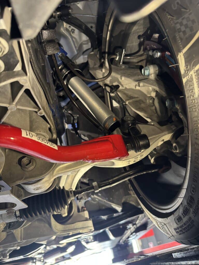 Close-up of a car wheel well showing suspension components, hoses, and bolts around the tire.