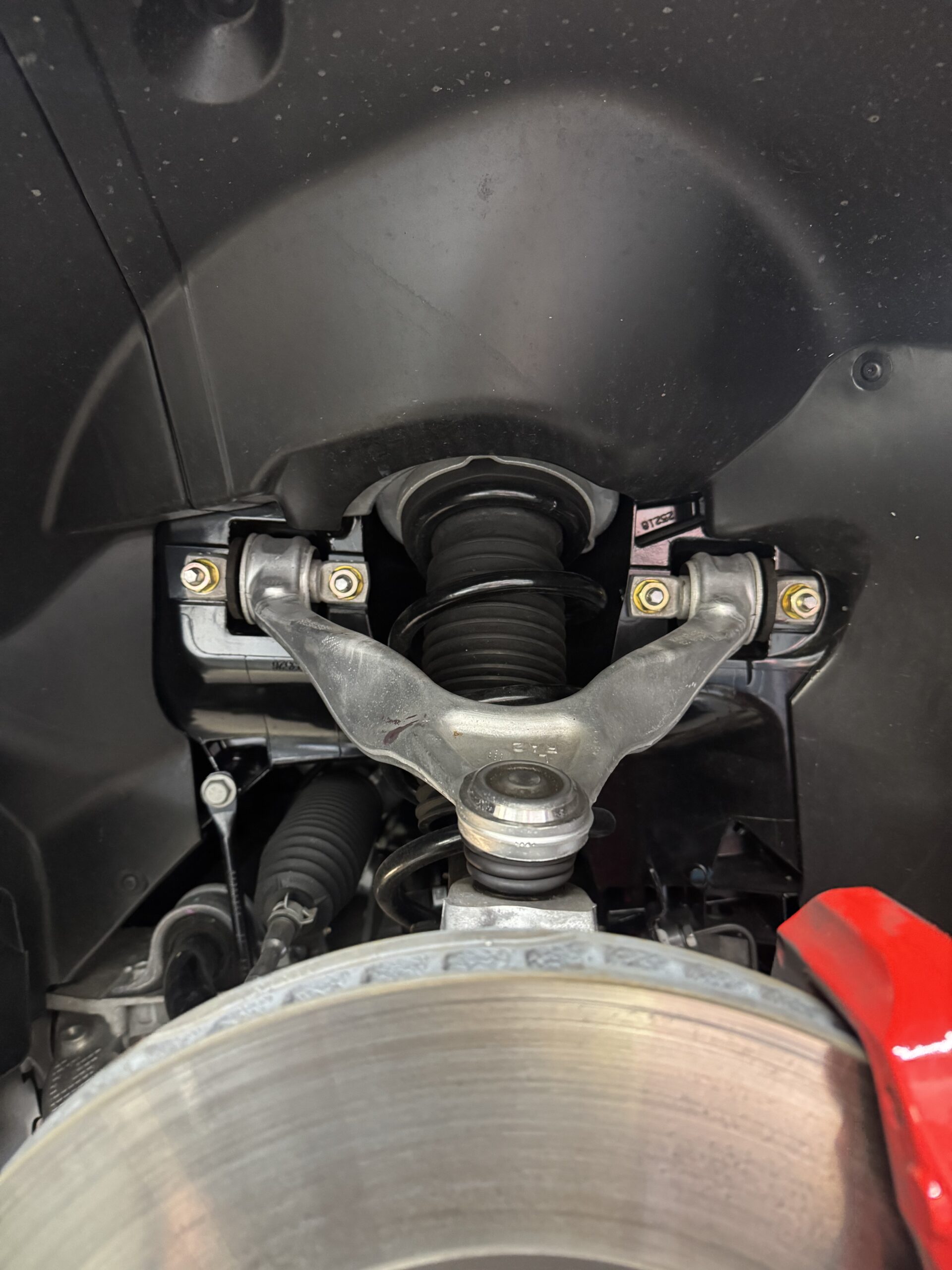 Close-up of a car's front suspension: coil spring, control arms, and brake caliper at the wheel hub area