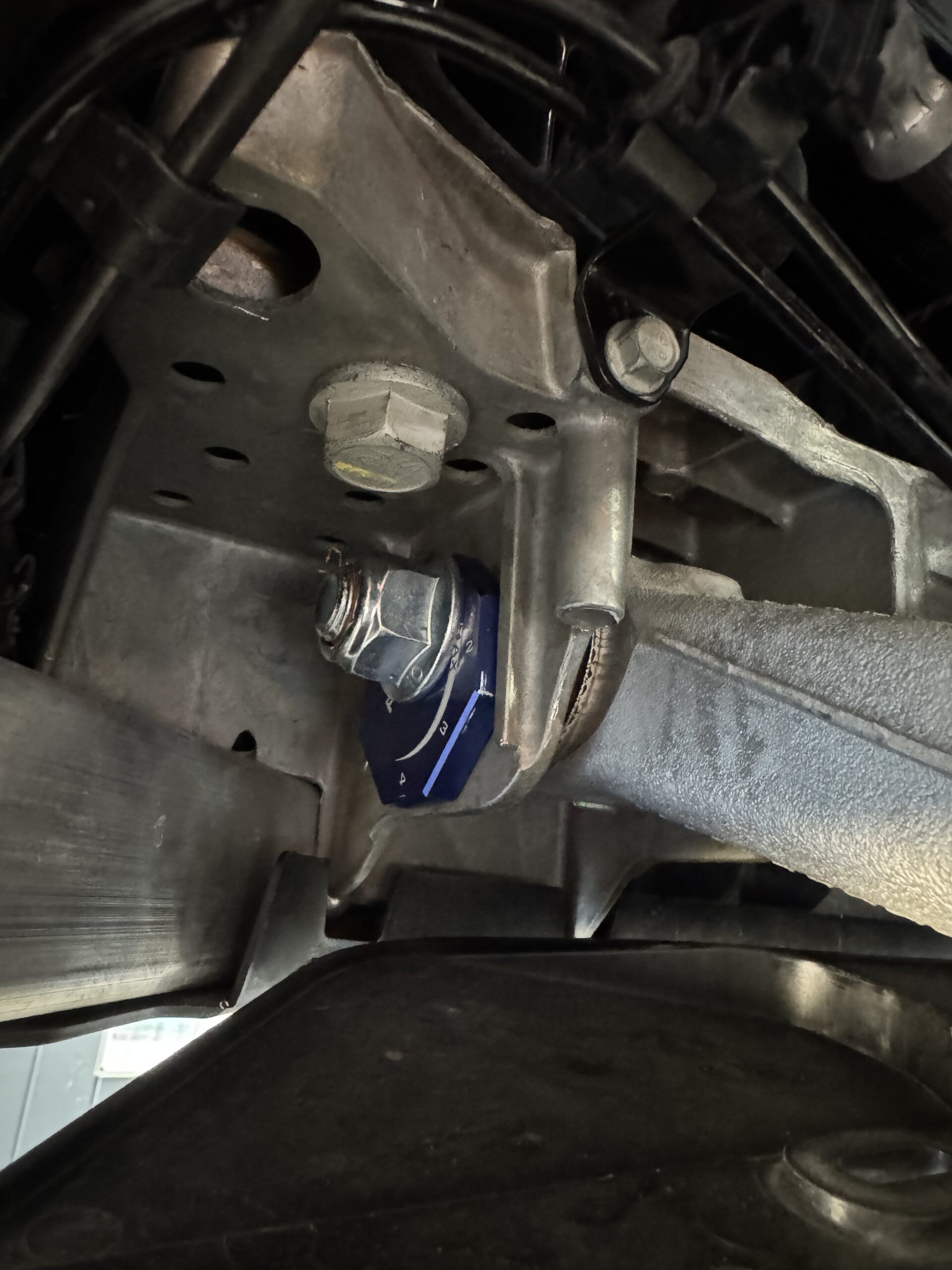 Close-up of a car's undercarriage showing a large hex bolt securing a metal bracket to the chassis, with wiring nearby.