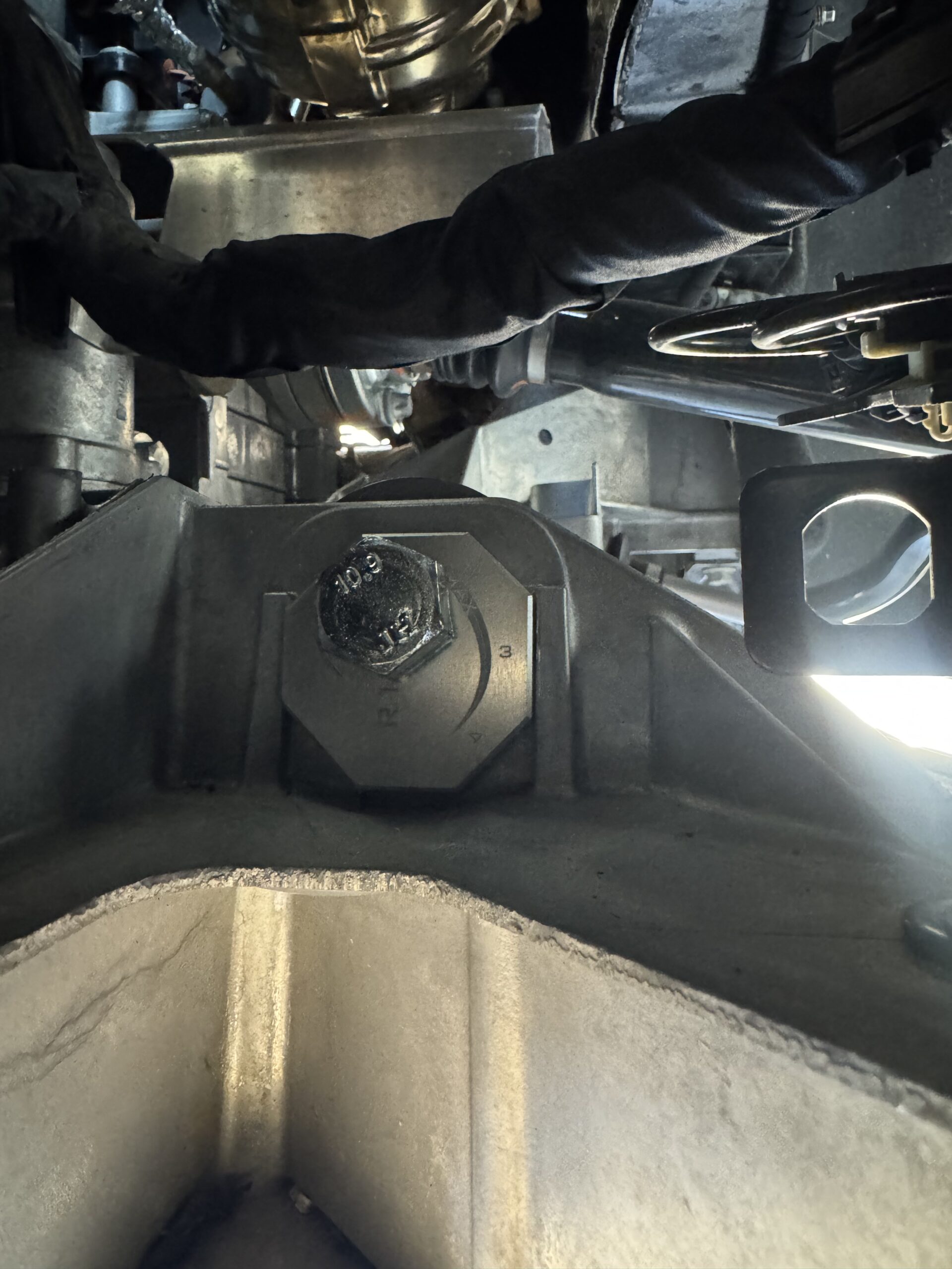 Underside of a vehicle showing a large hex bolt and surrounding metal framework.