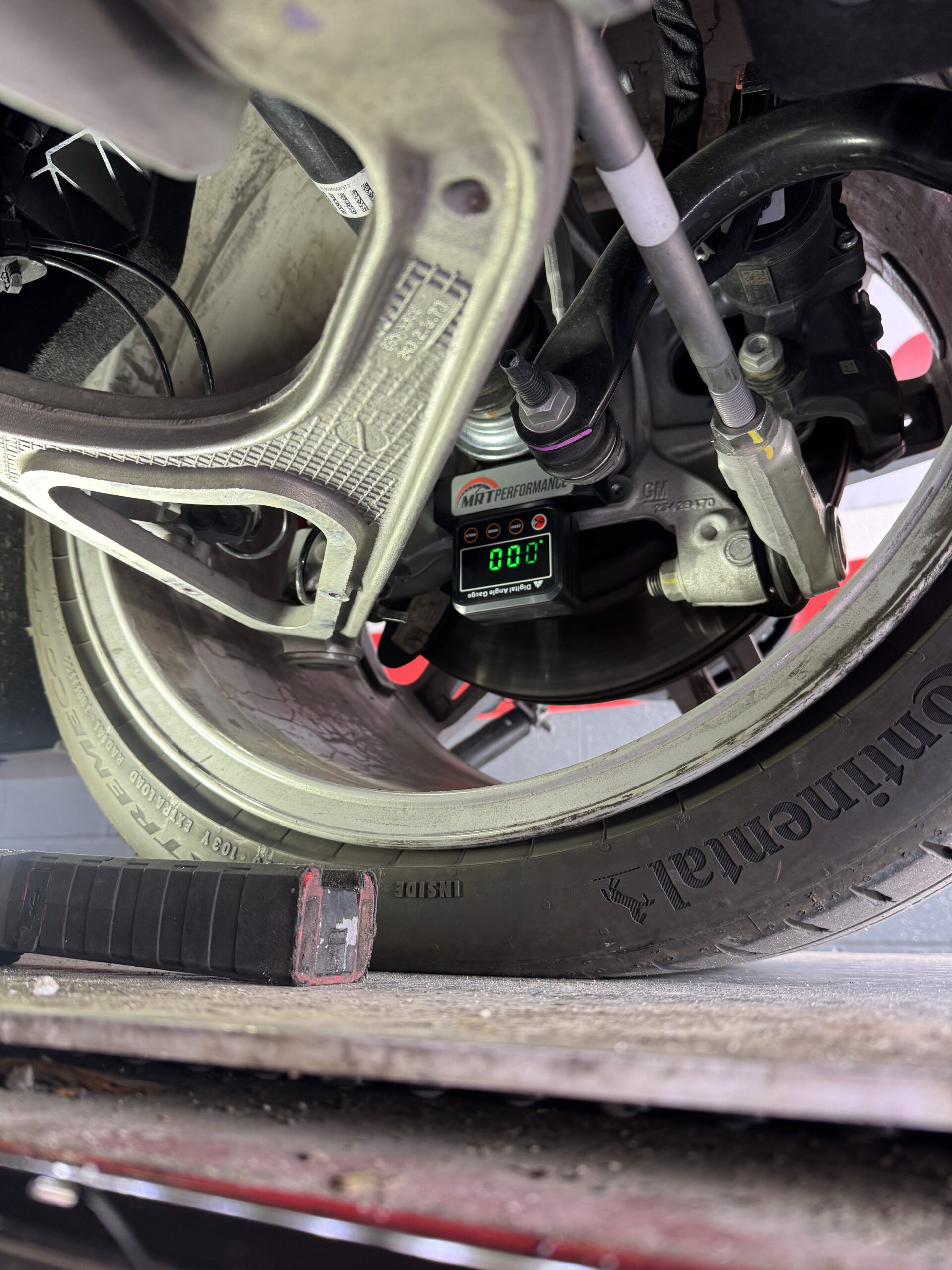 Close-up of a motorcycle rear wheel and suspension on a service stand, with a digital gauge displaying 0.0 at the bottom.