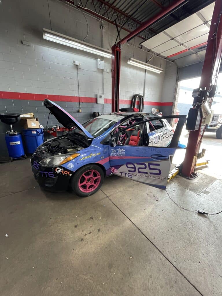 Blue race car with pink rims in a repair shop, hood open and garage equipment nearby (number 925).